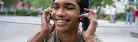 joyful african american man enjoying listening music in headphones outdoors, bannerの写真素材