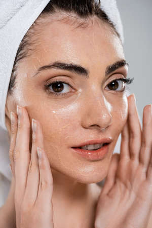 young woman with towel on head washing face and removing foundation isolated on grayの写真素材