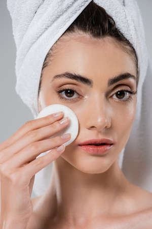 young woman with towel on head applying tonic with cotton pad isolated on grayの写真素材