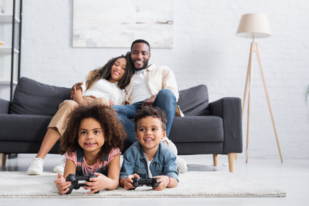KYIV, UKRAINE - JANUARY 25, 2021: blurred african american couple looking at kids gaming on floor