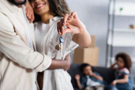 smiling african american woman holding key from new apartment near husband and blurred kidsの写真素材