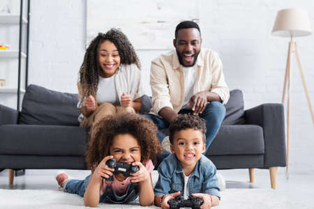 KYIV, UKRAINE - JANUARY 25, 2021: excited african american parents near kids playing video game on...