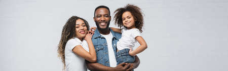 smiling african american man holding child near happy wife on gray, banner