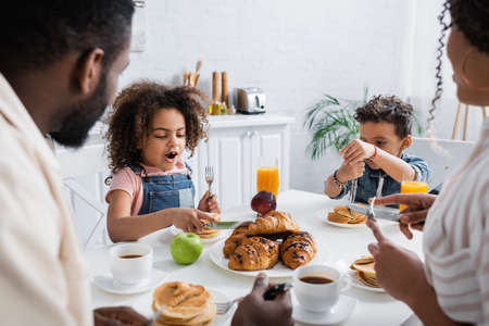 african american girl cutting croissant near brother and blurred parentsの写真素材