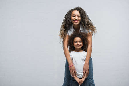 front view of african american woman with child looking at camera on gray