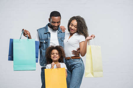 happy african american family holding multicolored shopping bags on grayの写真素材
