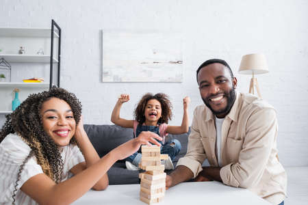 excited african american girl showing triumph gesture near smiling parent playing wood blocks gameの写真素材