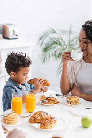 african american boy holding croissant near mom with cup of coffeeの写真素材