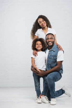 full length view of african american family embracing while smiling at camera on grayの写真素材