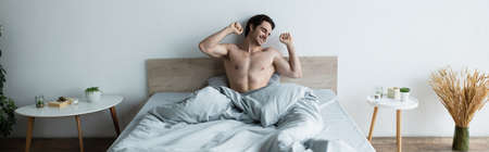 happy man stretching with closed eyes while sitting in bed, bannerの写真素材