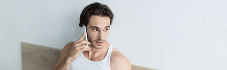 brunette man looking away while talking on smartphone in morning, banner