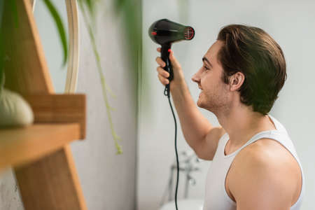 side view of smiling man drying hair in bathroomの写真素材