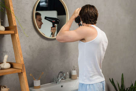 man in white tank top drying hair near mirror in bathroomの写真素材