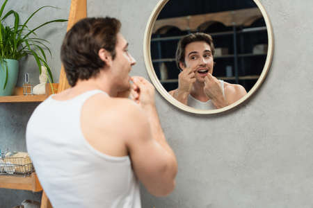 brunette man in white tank top cleaning teeth in bathroom near mirrorの写真素材