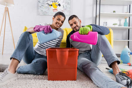 Smiling african american woman pouring detergent in bucket near boyfriendの写真素材