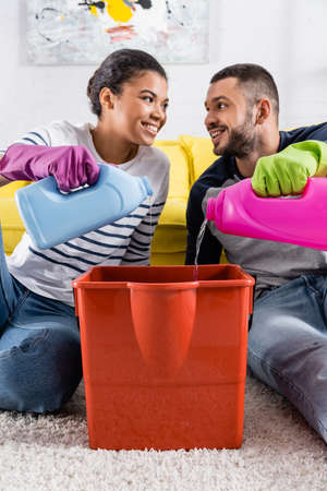 Smiling interracial couple pouring detergents in bucketの写真素材