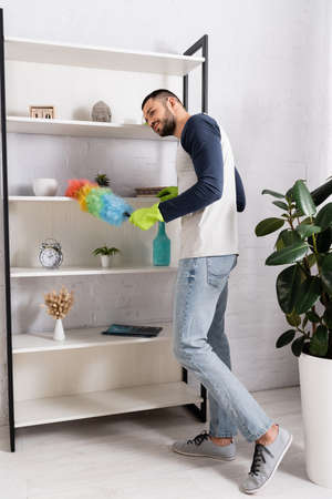 Young man cleaning cupboard with dust brush