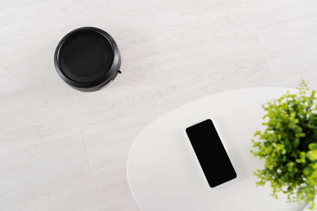 Top view of robotic vacuum cleaner on floor near smartphone on coffee tableの写真素材