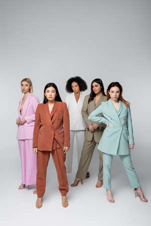 full length of multiethnic models in stylish suits posing isolated on grayの写真素材