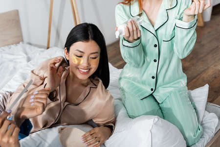 cheerful asian woman with eye patches smiling near friends during slumber party