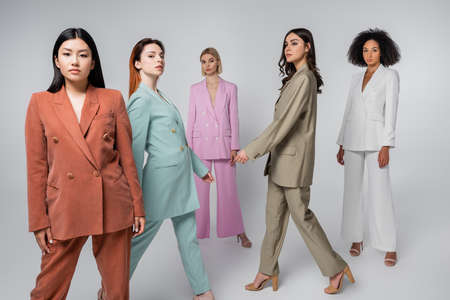 full length of interracial models in stylish suits walking on grayの写真素材