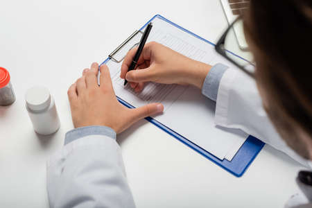 partial view of blurred physician writing on clipboard near containers with treatment, medical cannabis conceptの写真素材
