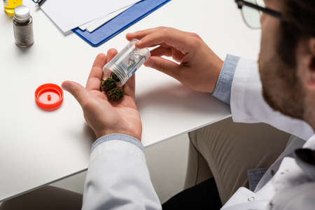 cropped view of blurred doctor holding dry medical hemp near white desk