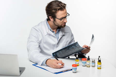 doctor writing prescription while holding mri scan near containers with medical cannabis isolated on...