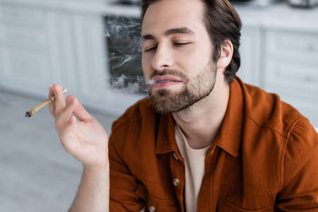 Bearded man smoking cigarette of medical cannabis at homeの写真素材