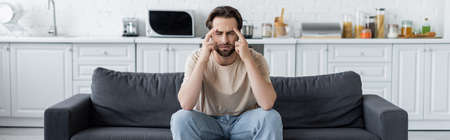 Man suffering from headache on couch in kitchen, banner