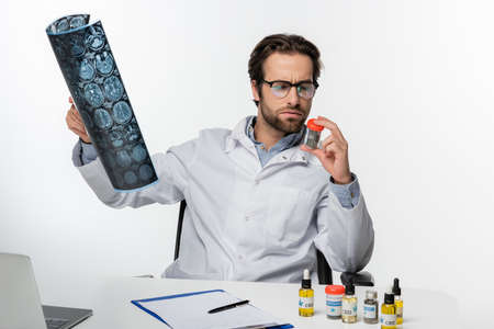 serious doctor with mri scan and container of dry medical cannabis isolated on whiteの写真素材