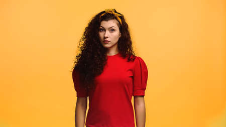 discouraged woman with wavy hair looking at camera isolated on orangeの写真素材