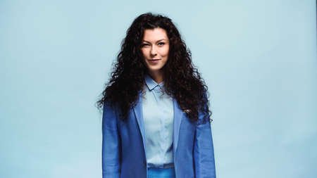 positive woman in blue blazer smiling at camera isolated on blue