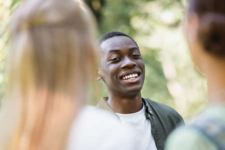 Smiling african american teenager looking at camera near blurred friendsの写真素材