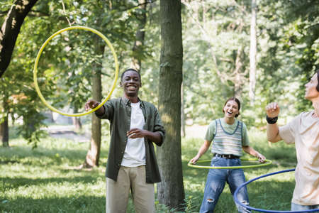 Smiling african american teenager holding hoop near friends in park