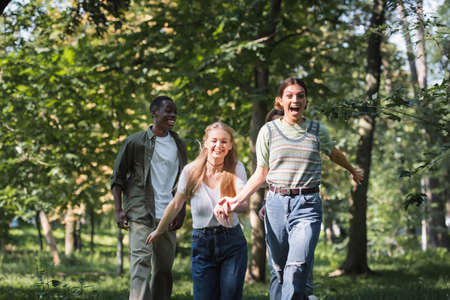 Cheerful teen girls running near multiethnic friends in parkの写真素材
