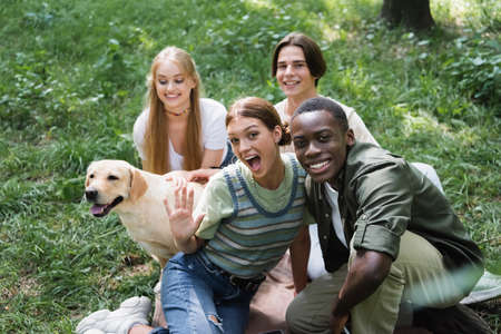 Happy multiethnic teen friends looking at camera near retriever on lawnの写真素材