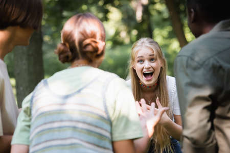 Excited teen girl looking at blurred interracial friendsの写真素材