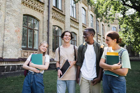 Positive multiethnic students with laptop and backpacks outdoorsの写真素材