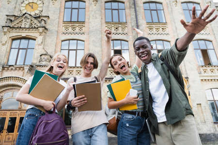 Low angle view of excited interracial students with notebooks looking at camera outdoorsの写真素材