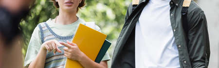 Cropped view of student with notebooks pointing with finger near friend outdoors, bannerの写真素材