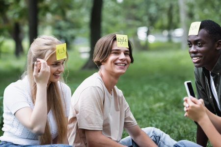 Positive multiethnic teenagers with smartphone playing who i am in parkの写真素材