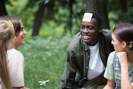 Cheerful interracial teenagers with stickers playing who i am in park