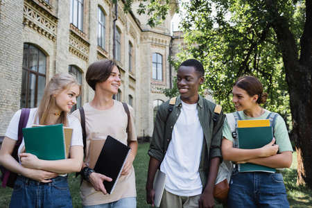 Smiling multiethnic students with laptop and notebooks outdoorsの写真素材
