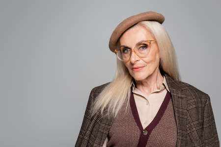 Stylish senior woman in plaid jacket and beret looking at camera isolated on grayの写真素材