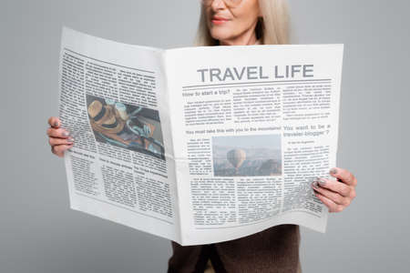 Cropped view of blurred senior woman holding travel newspaper isolated on grayの写真素材