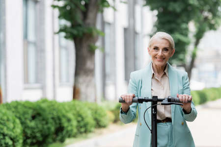 senior businesswoman with electric kick scooter smiling at camera on streetの写真素材