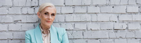 Senior businesswoman looking at camera near brick wall, banner