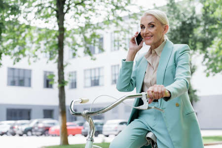 senior business lady talking on mobile phone while sitting on bike outdoorsの写真素材