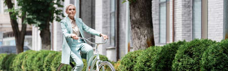 elderly business lady in suit cycling on urban street, bannerの写真素材